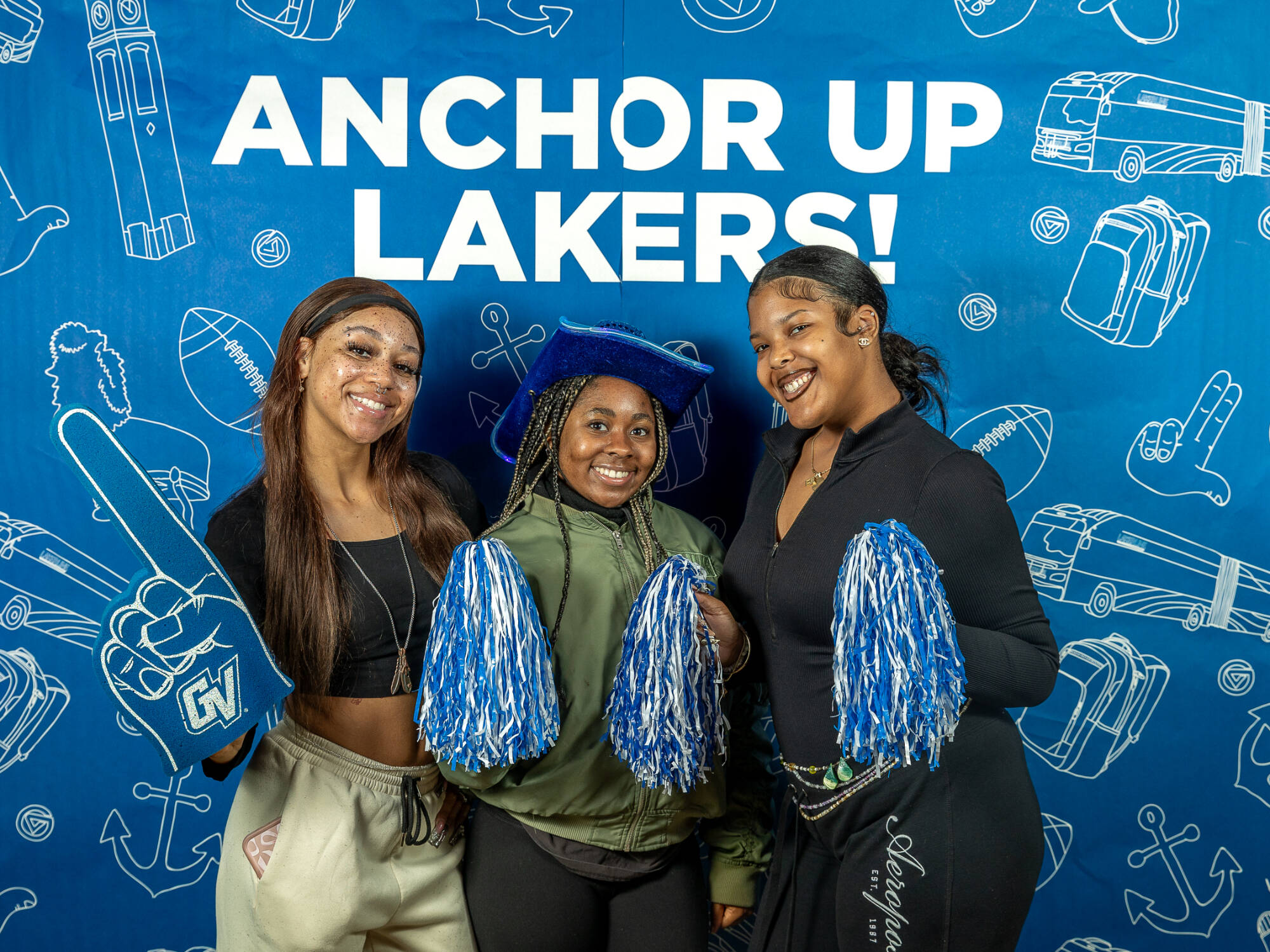 three individuals, one on the left holding up a foam finger, one in the middle holding up two pompoms wearing a blue cowboy hat, one on the right also holding up a pompom